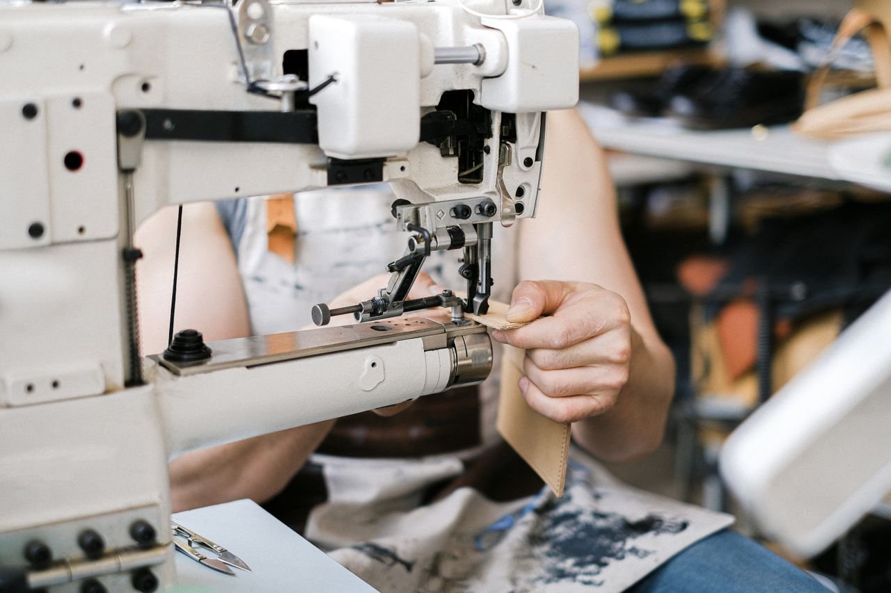 services-01 An artisan carefully stitches leather using a professional sewing machine in a workshop setting.